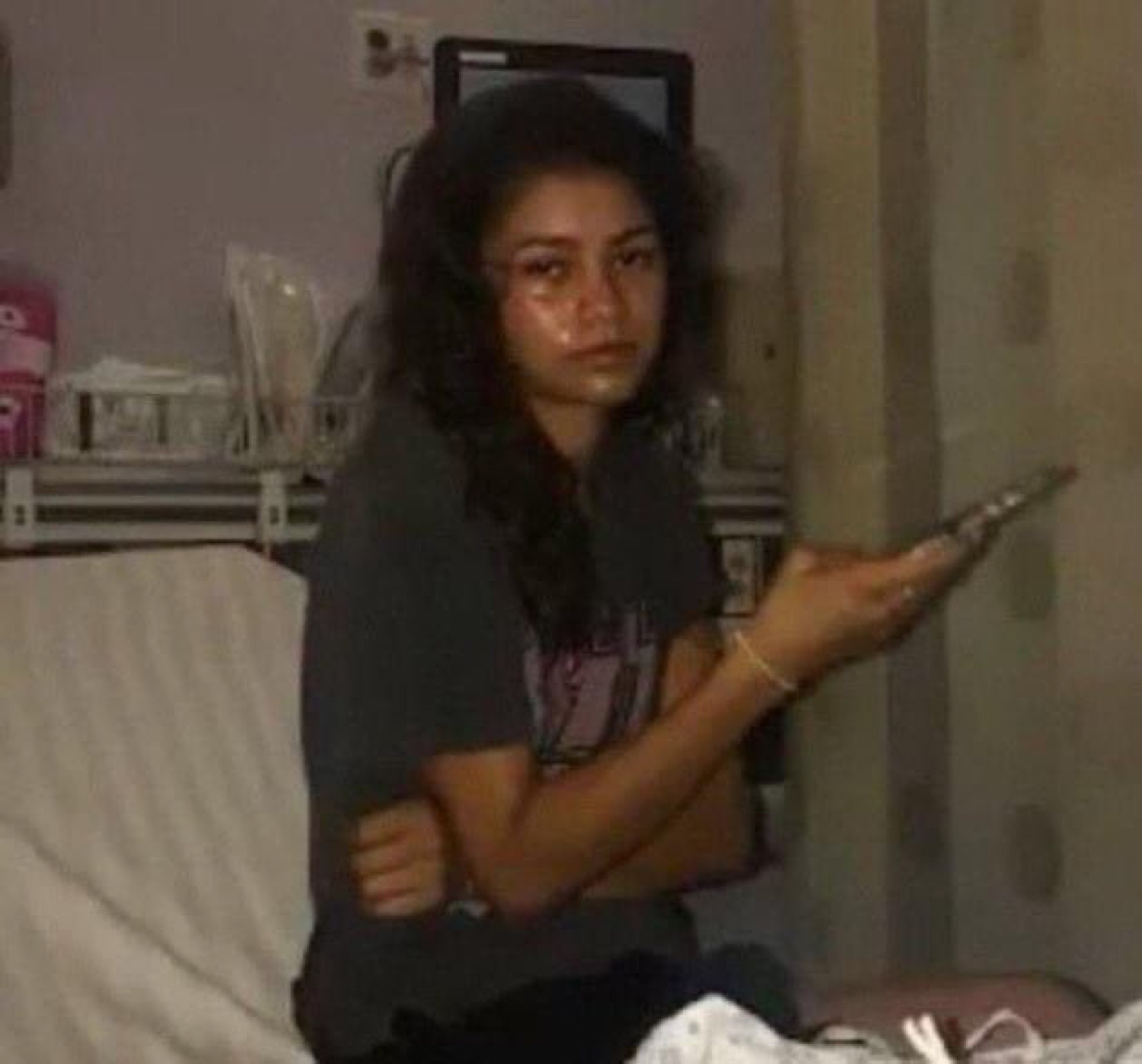 Teary young woman sitting on a bed pointing a phone at the camera with a fed-up look