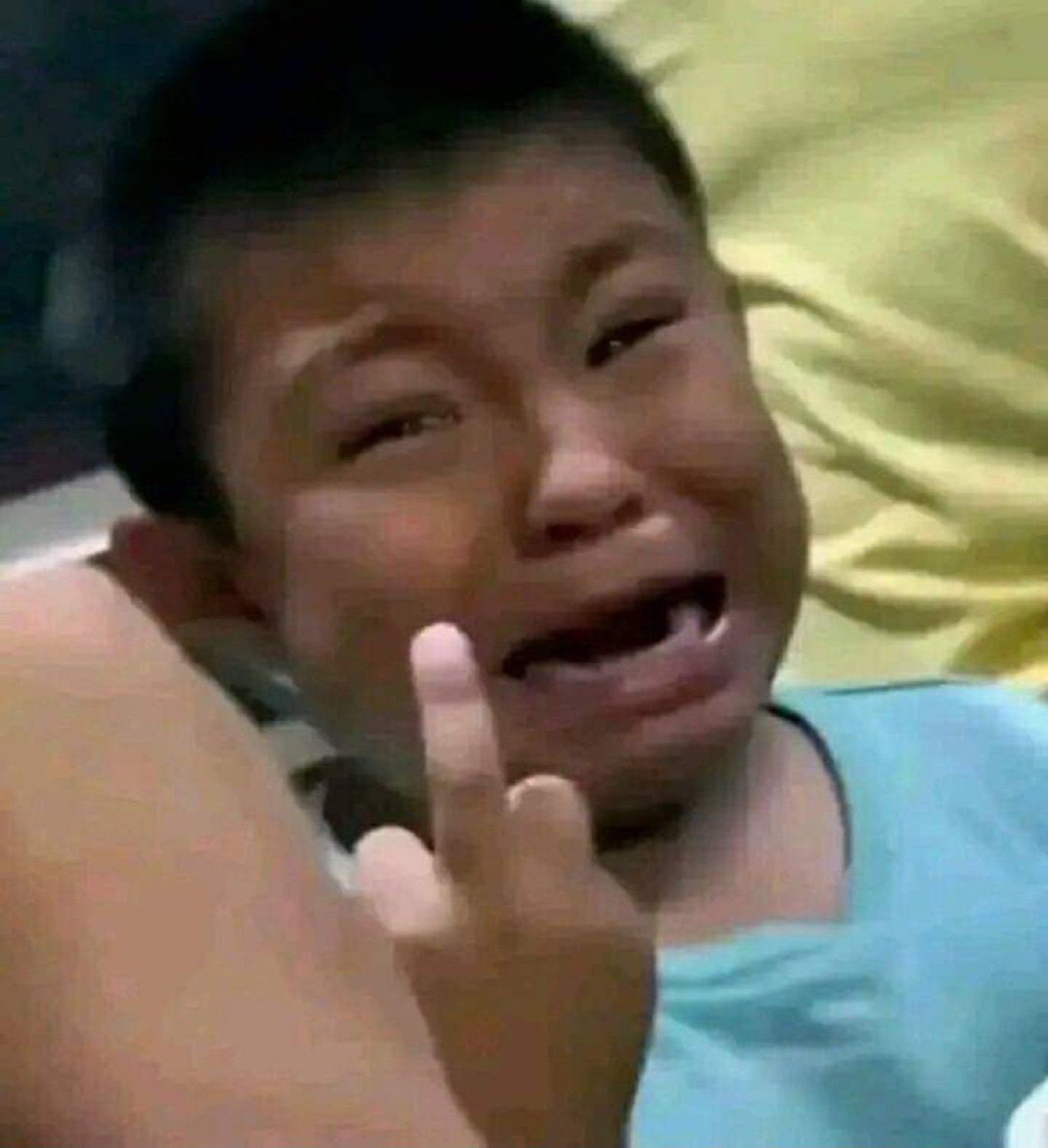 Crying kid throwing up a defiant hand gesture while sobbing on a bed
