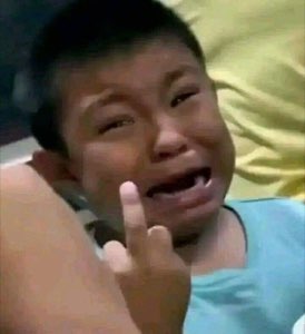 Crying kid throwing up a defiant hand gesture while sobbing on a bed