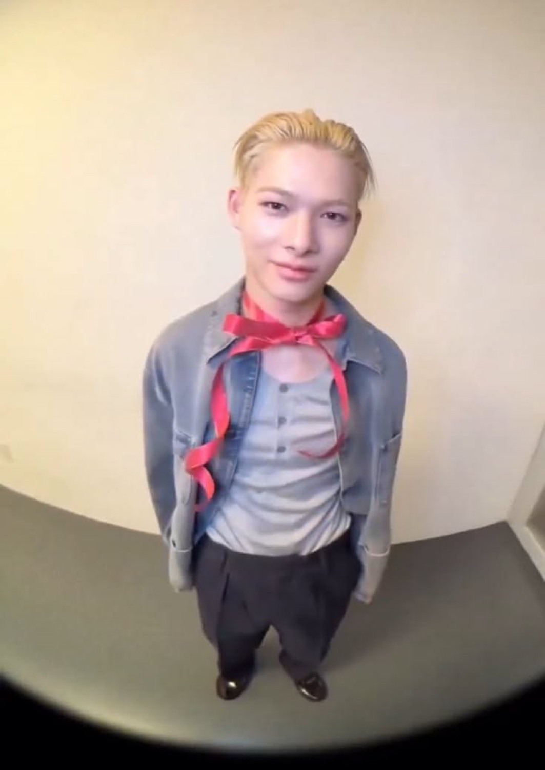 Blond guy with a red ribbon tied around him shot from above with a tight little smile