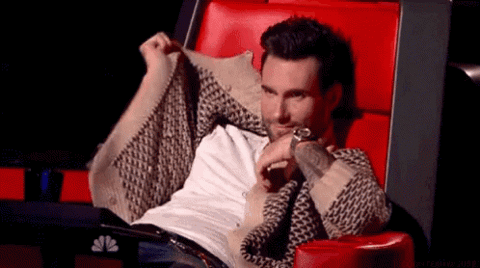 Adam Levine in a red chair on The Voice burying his face in his hands