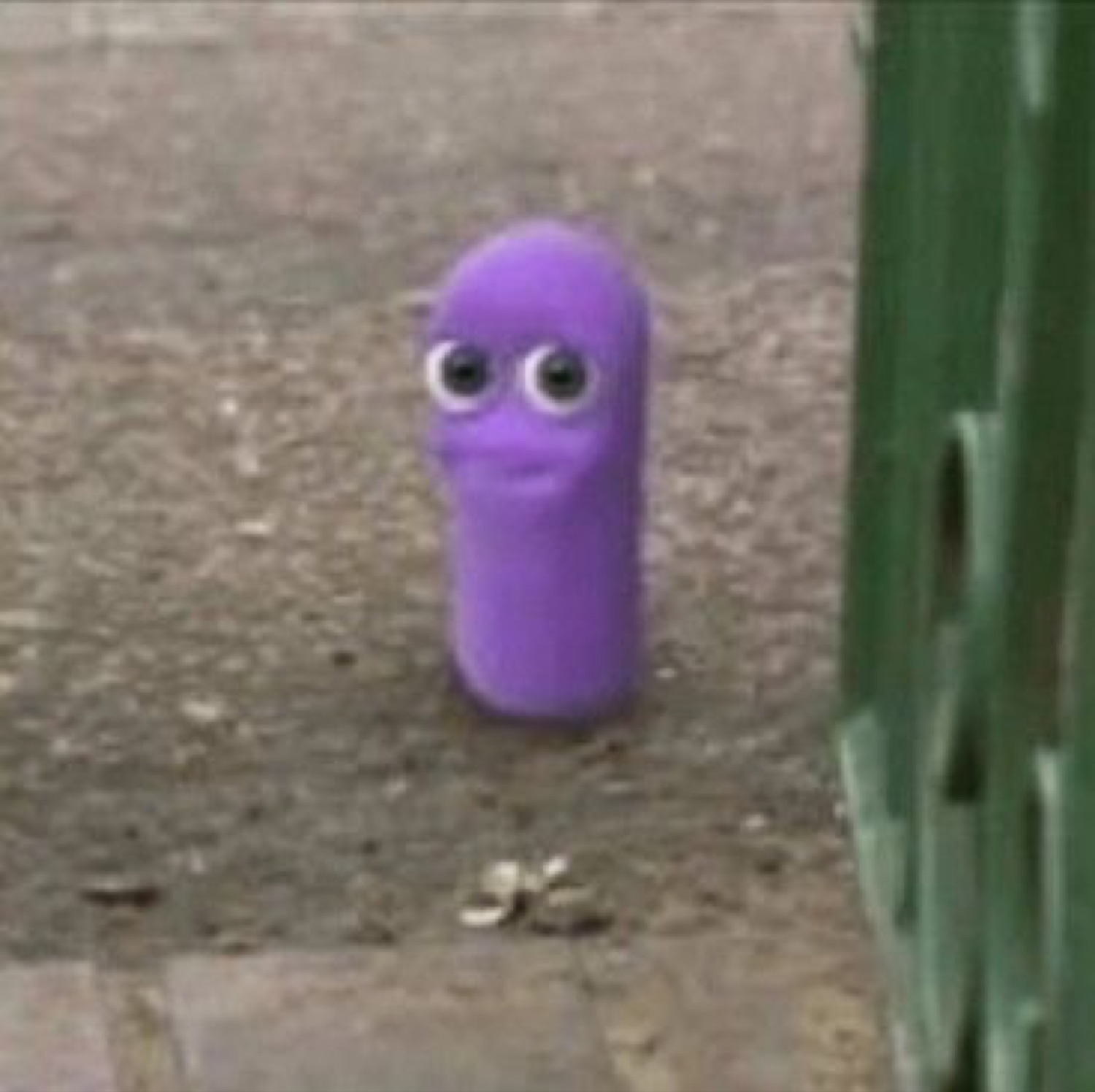 Little purple puppet with googly eyes standing still on a sidewalk