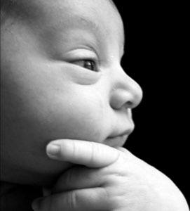 Black-and-white close-up of a baby resting its chin on its hand with a pensive, thoughtful look