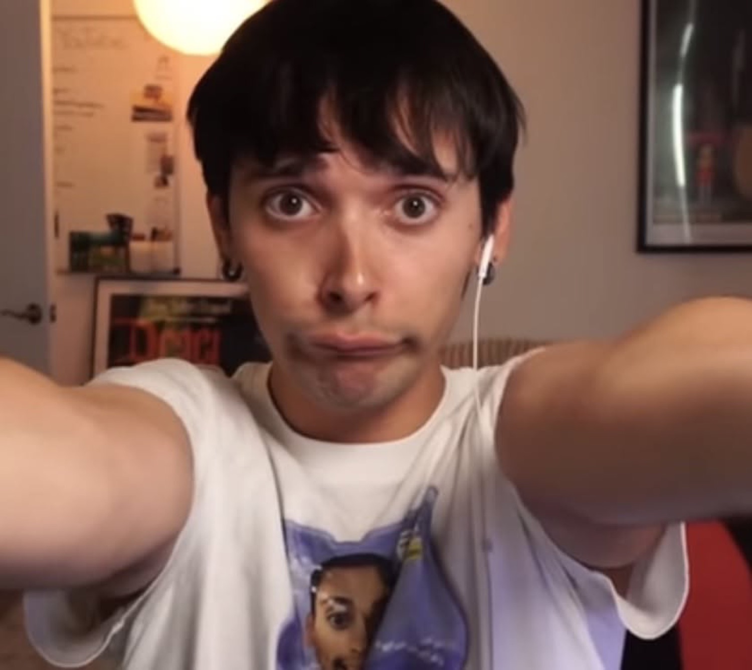 Young man reaching toward the camera with earbuds in and an awkward blank face