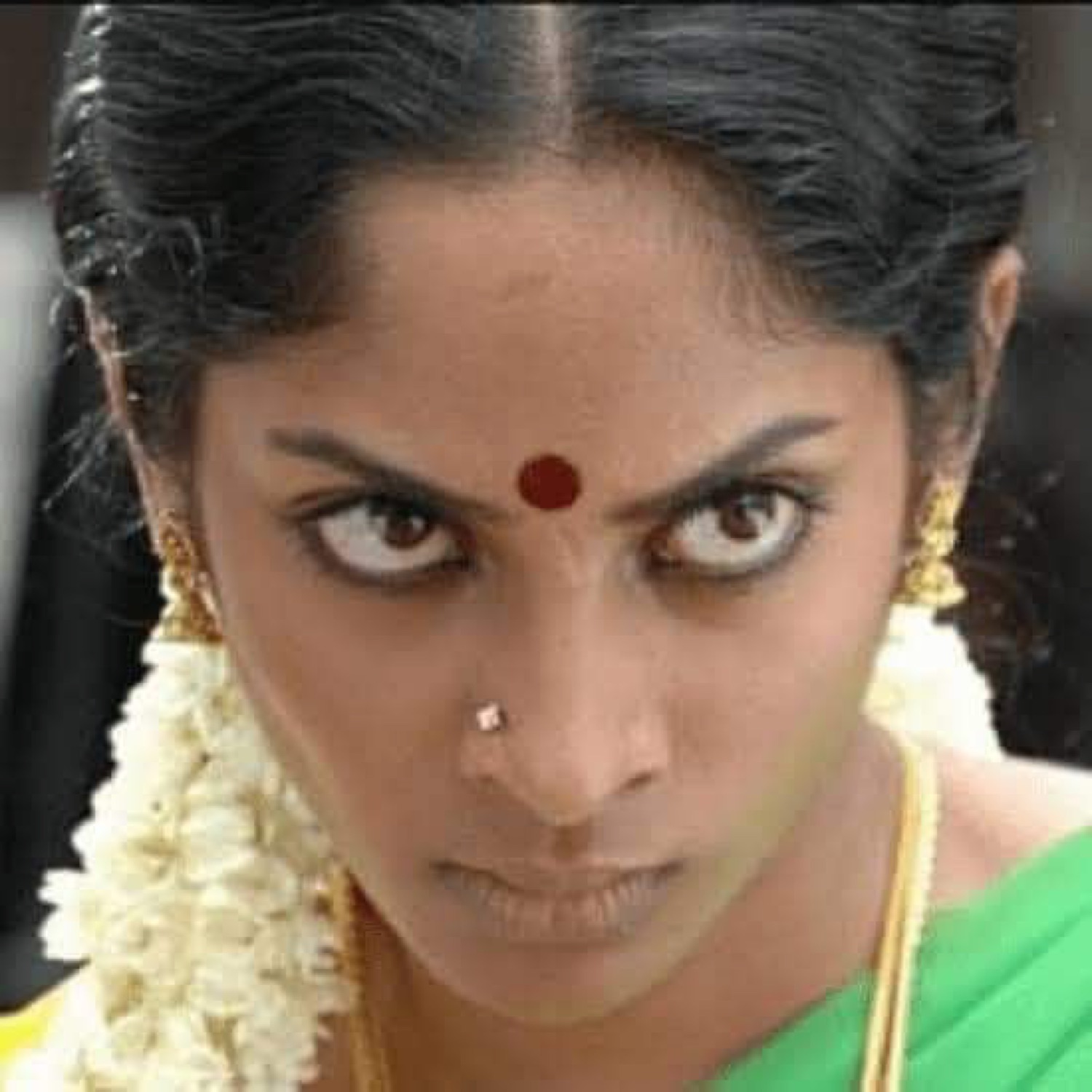 Woman in a jasmine garland glaring with wide furious eyes