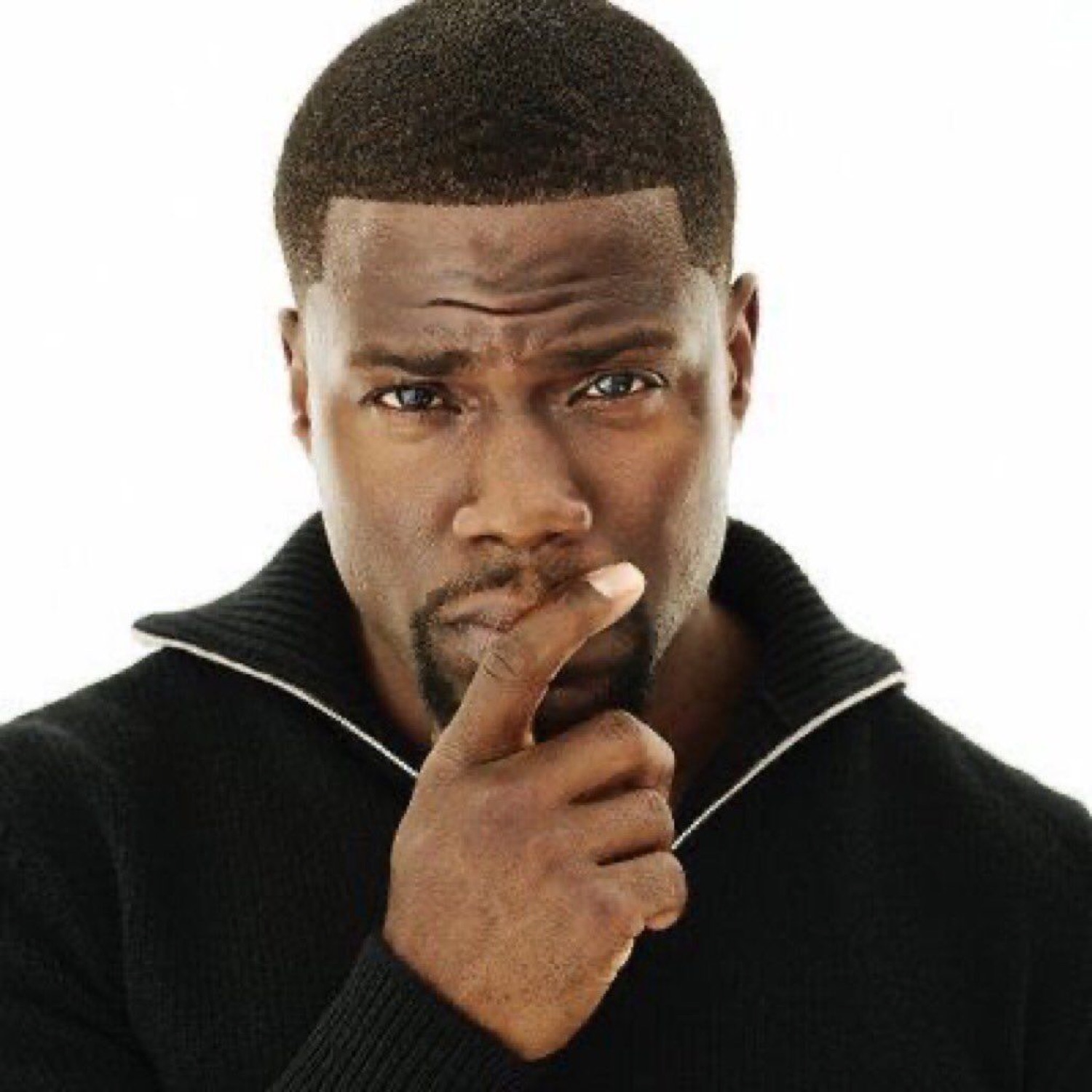 Kevin Hart in a black sweater resting his thumb on his lips with a skeptical, thinking look