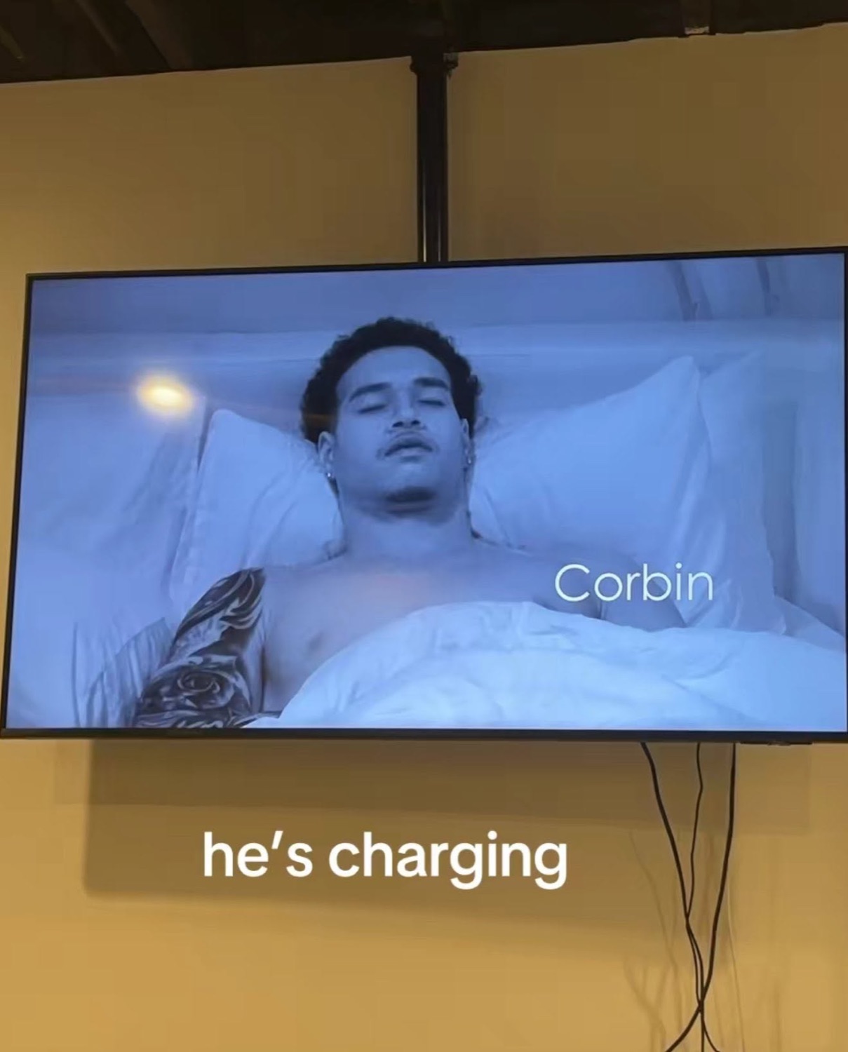TV showing Love Island USA's Corbin asleep in bed, labeled 'Corbin', under 'he's charging'