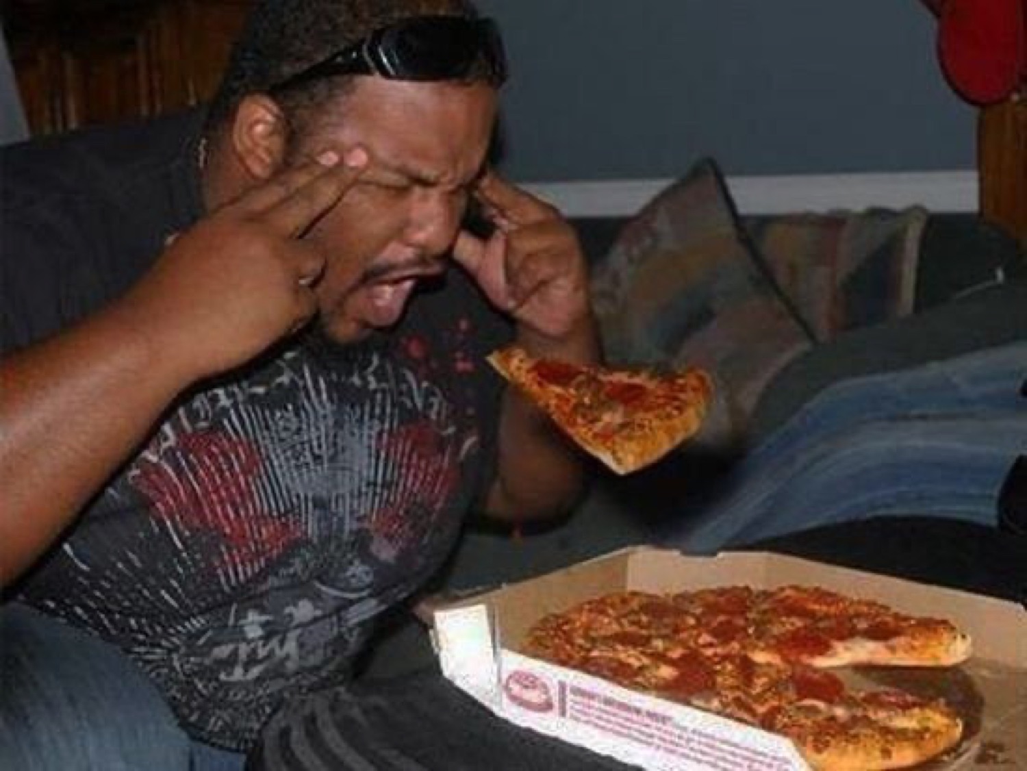 Man pressing both index fingers to his temples with eyes wide open eating pizza in a revelation moment