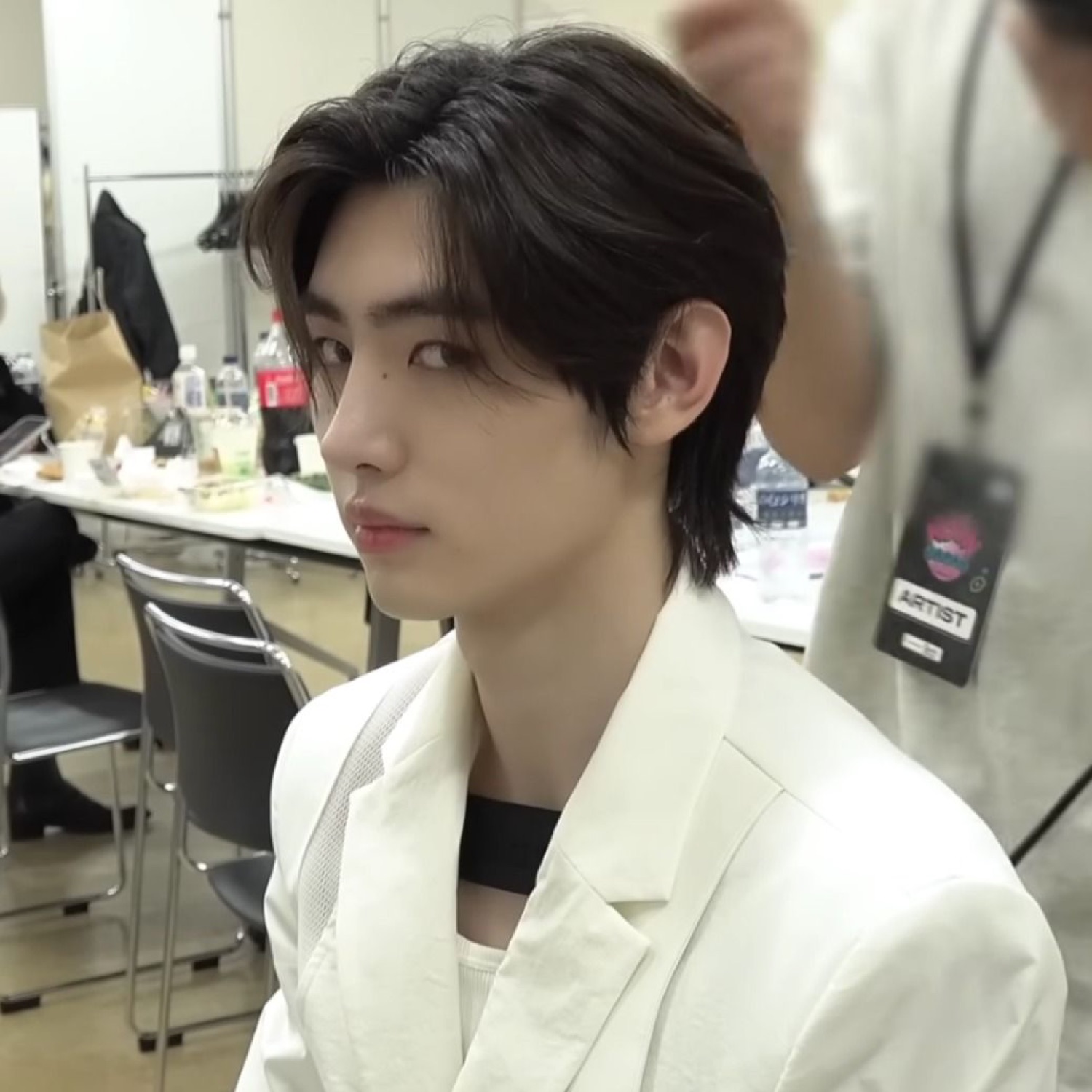 Guy in a white blazer backstage giving a flat sideways glance