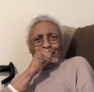 Elderly woman in glasses resting her fist against her lips with a knowing look