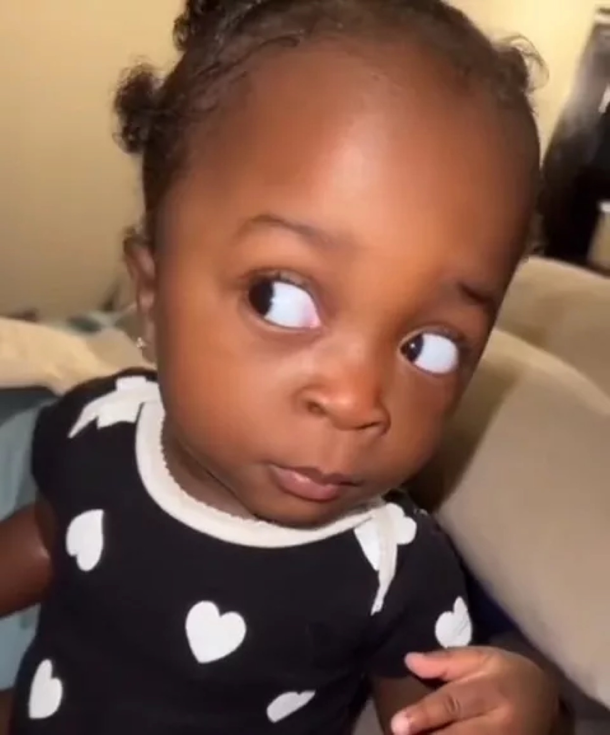 Baby in a heart-print onesie throwing a slow, doubtful side-eye