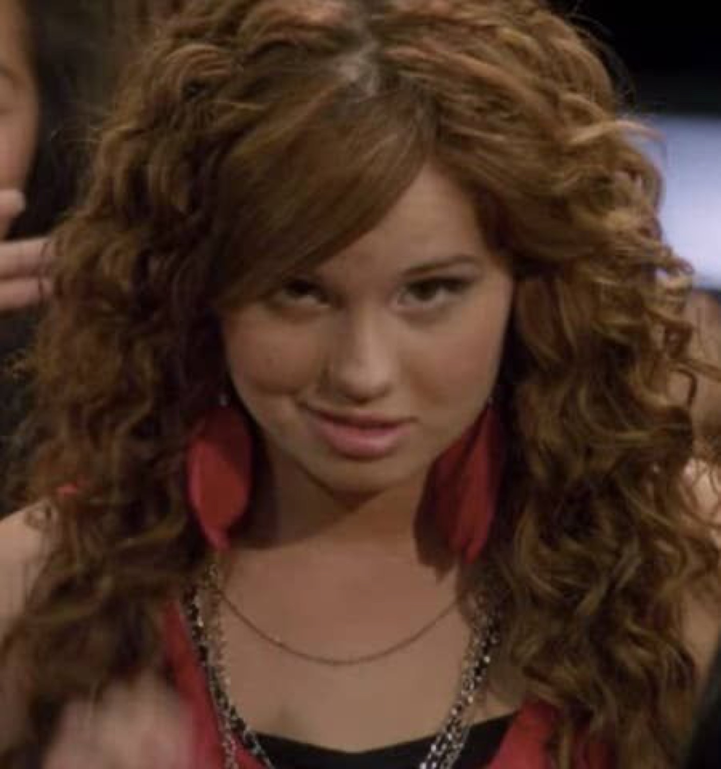 Curly-haired girl in red giving a slow, knowing smirk to the side