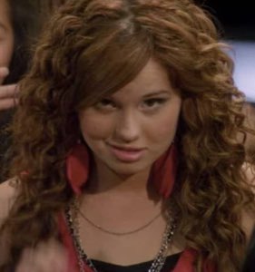 Curly-haired girl in red giving a slow, knowing smirk to the side