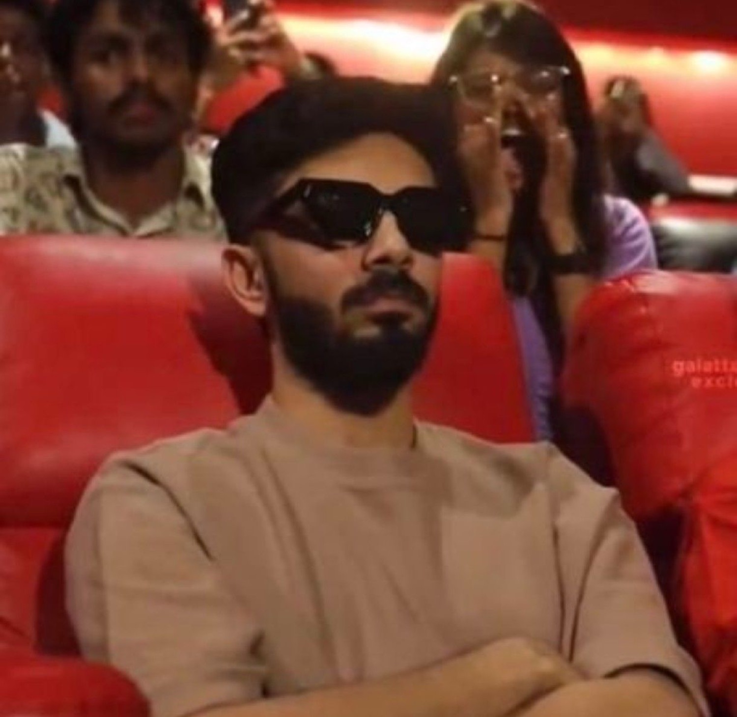 Man in sunglasses in a cinema with people cheering behind him