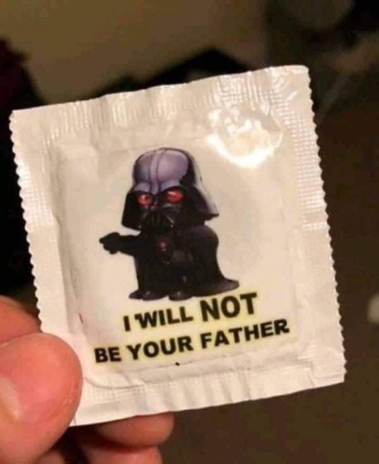Hand holding a condom wrapper with chibi Darth Vader reading 'I WILL NOT BE YOUR FATHER'