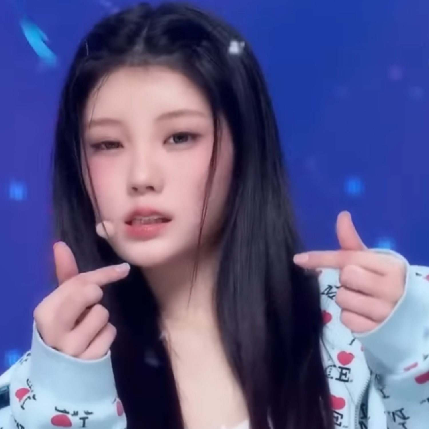 K-pop idol on stage throwing lazy finger hearts with a completely blank face