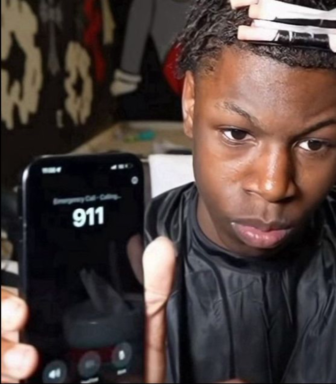 Young man at a barber staring intensely while holding up a phone showing a 911 call