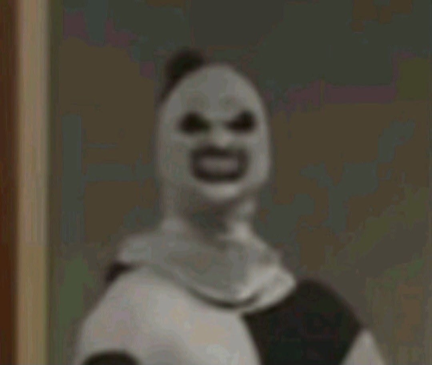 Grainy figure in a pale mask grinning eerily straight at the camera