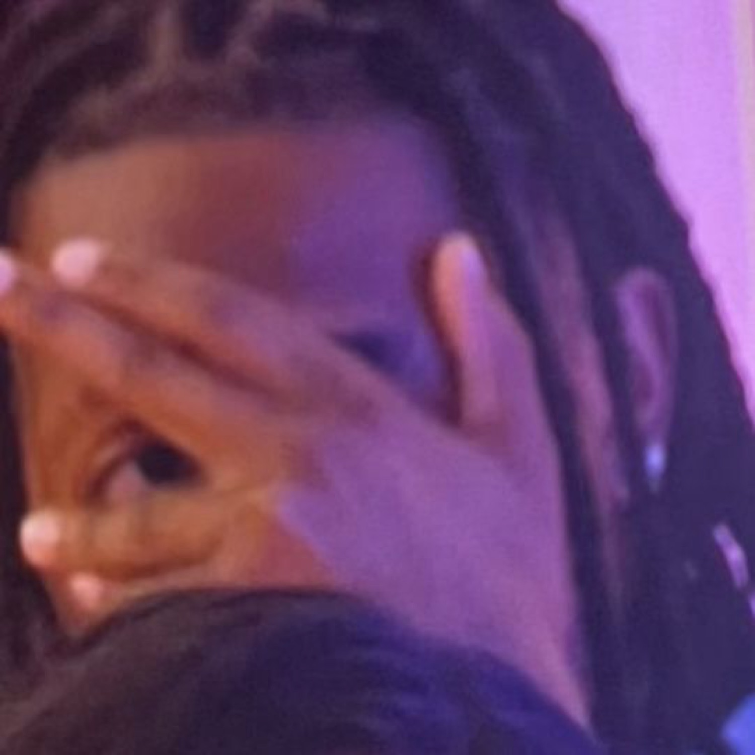 Person with locs pressing their hand over their face in a full-on facepalm under purple light