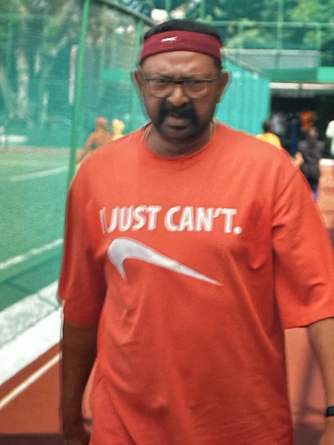 Man in a red 'JUST CAN'T' shirt looking exhausted
