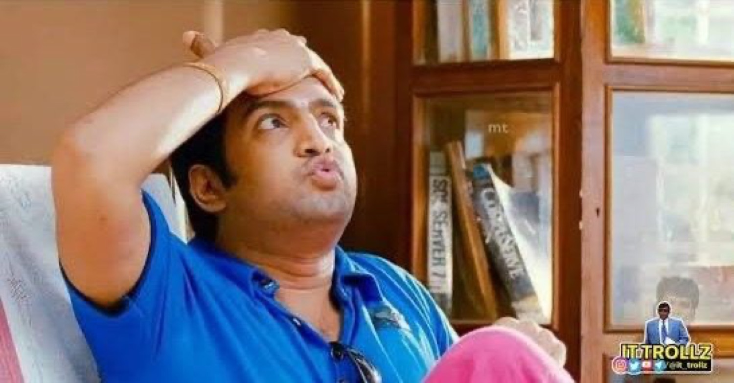 Santhanam on a couch rubbing his head and blowing out air