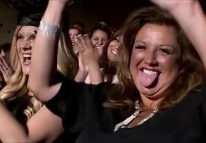 Woman in a crowd clapping and sticking her tongue out mid-celebration