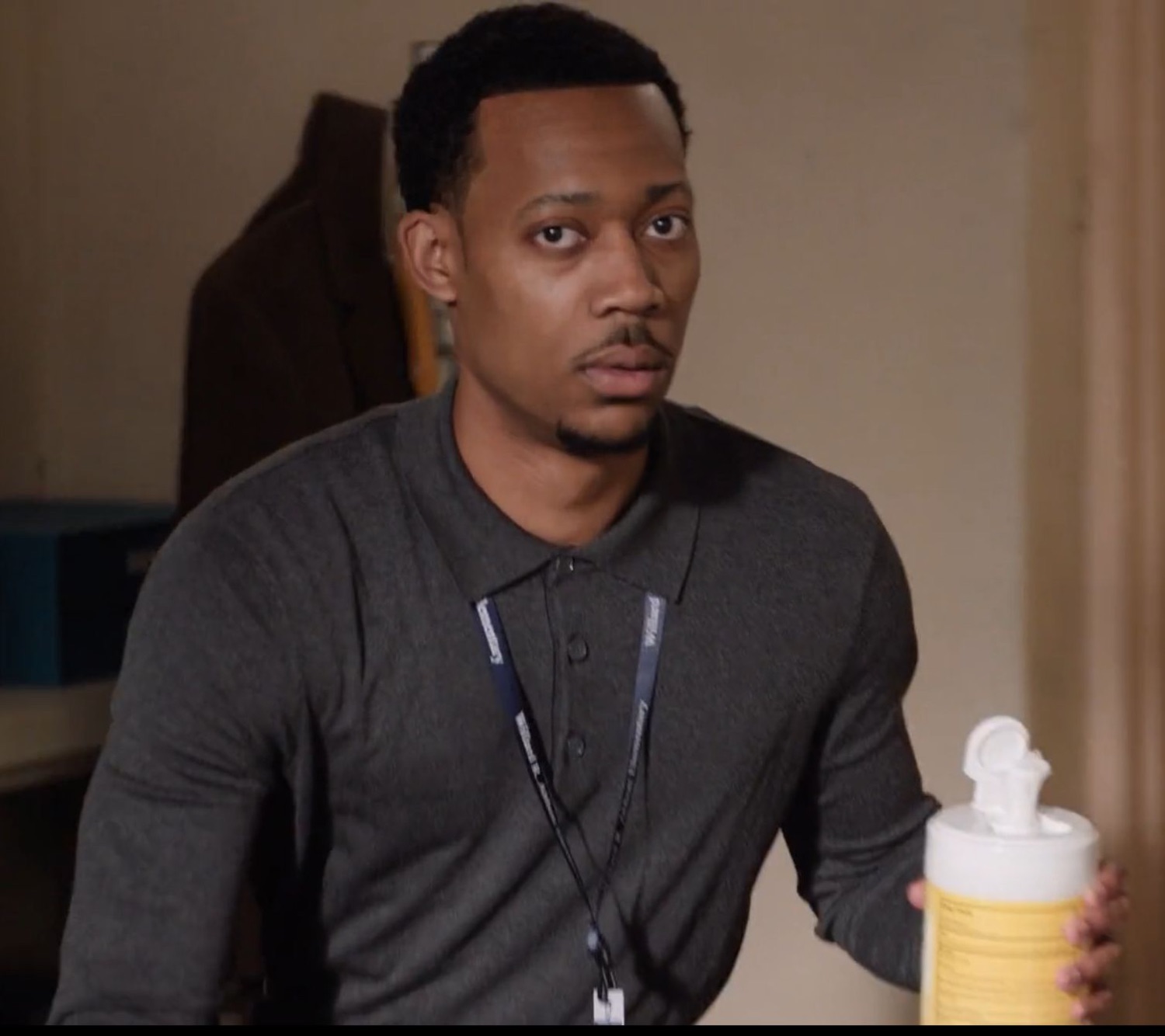 Man in a polo shirt holding a container of wipes, looking sideways with a baffled expression