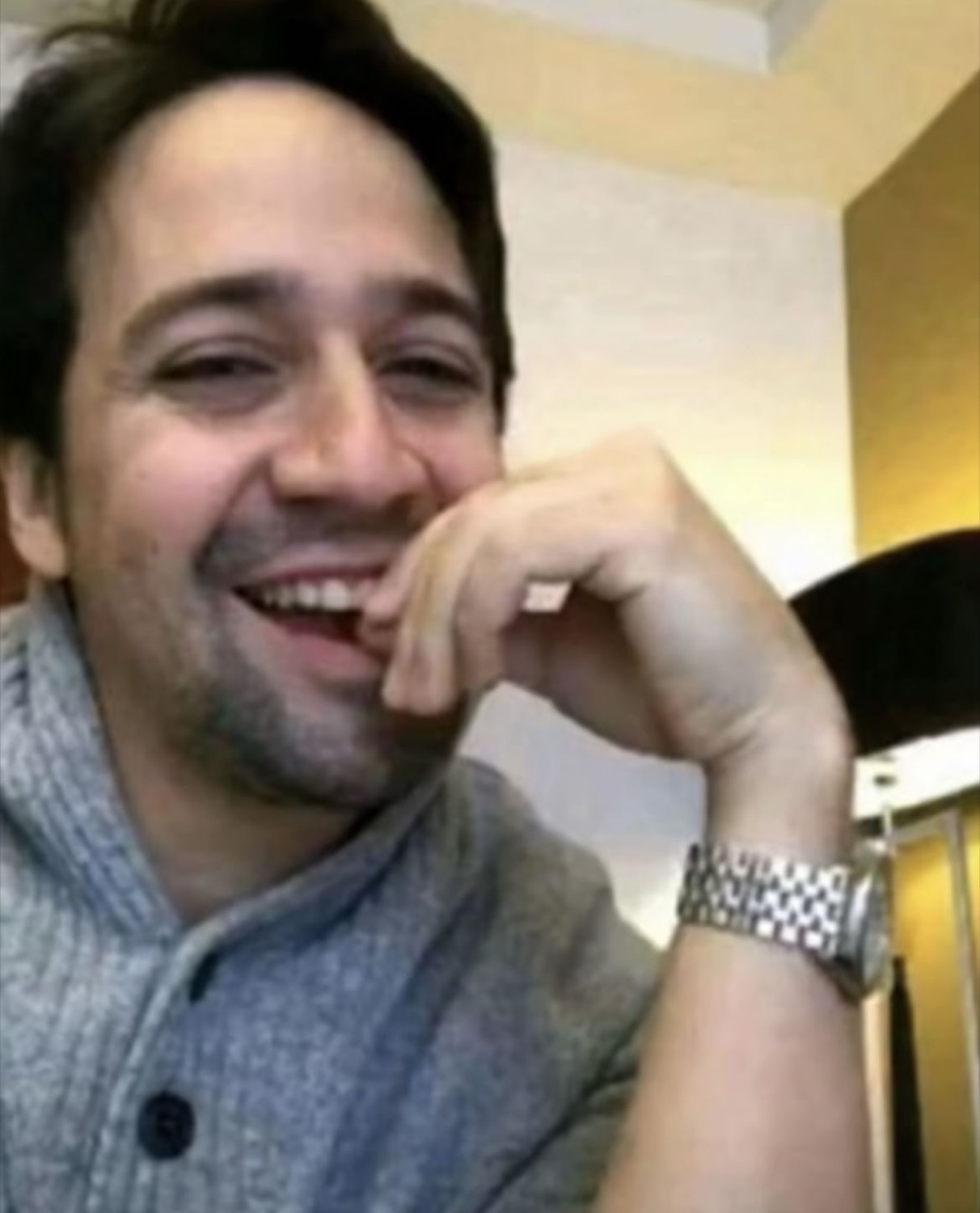 Man in a grey sweater laughing and covering his mouth with his hand