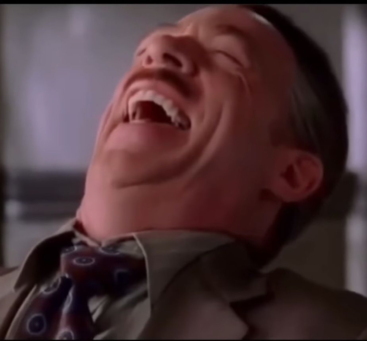 Man in a suit throwing his head back in a full, uncontrollable laugh