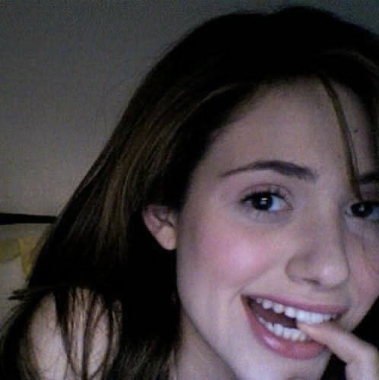 Young woman beaming with a playful grin, finger at her lip