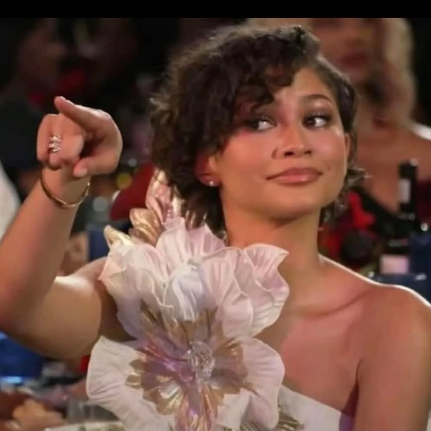 Glamorous woman in floral dress pointing with a knowing smirk at an event