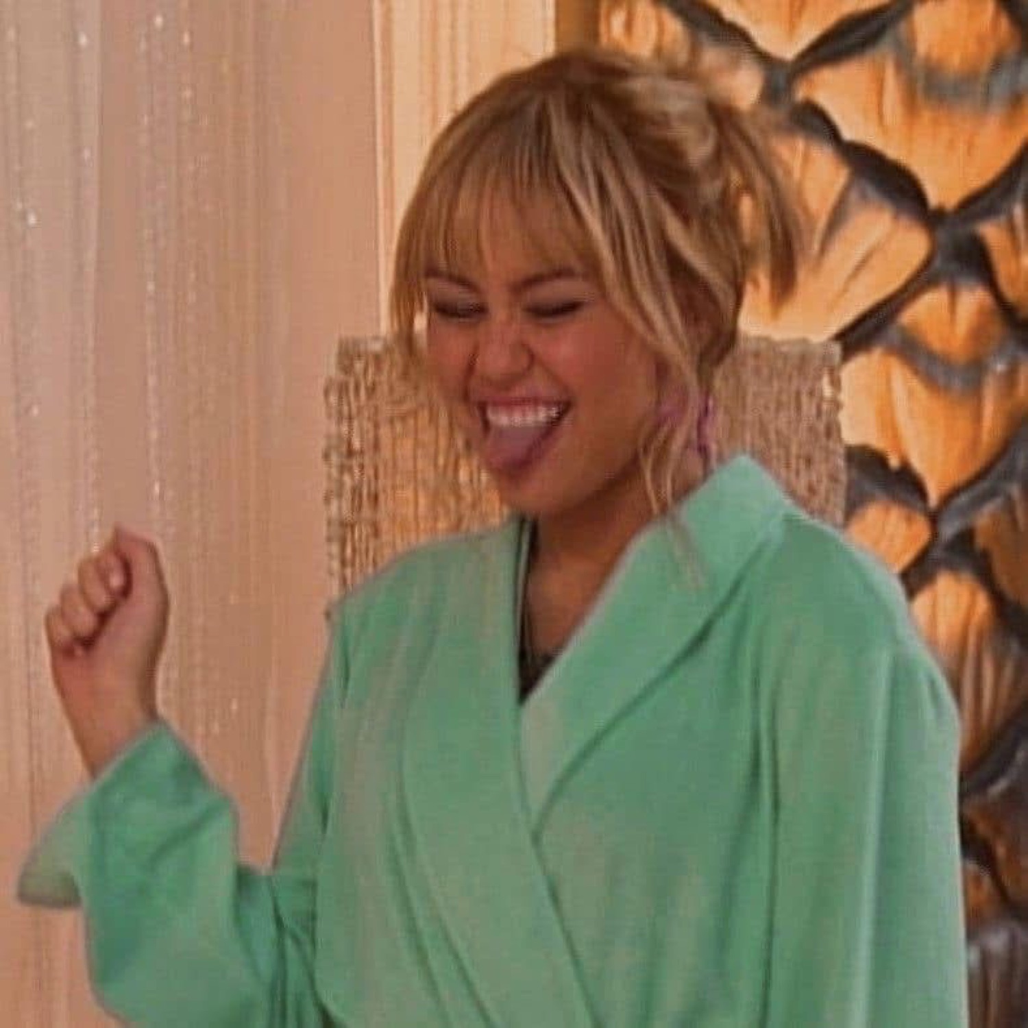 Blonde woman in a mint green robe pumping her fist and laughing with pure joy