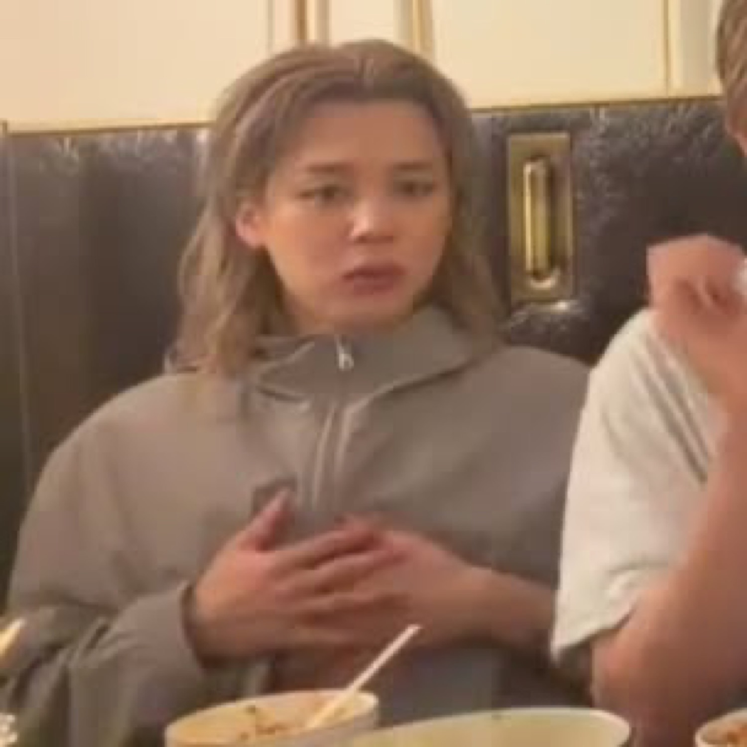 Young woman at a restaurant table gesturing while making a puzzled, uneasy face