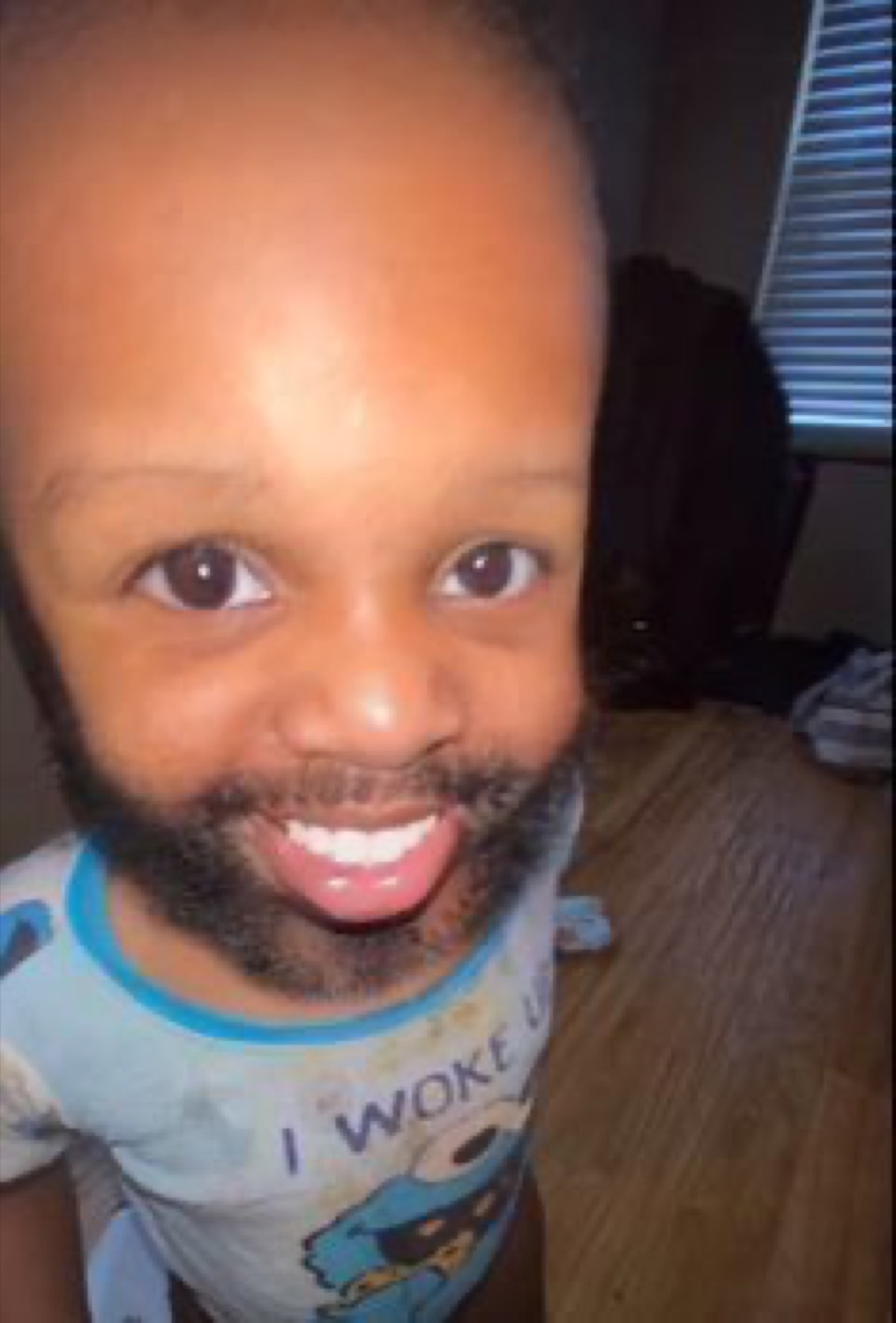 Baby with a man's beard photoshopped on, grinning with tongue out, shirt reading 'I WOKE'
