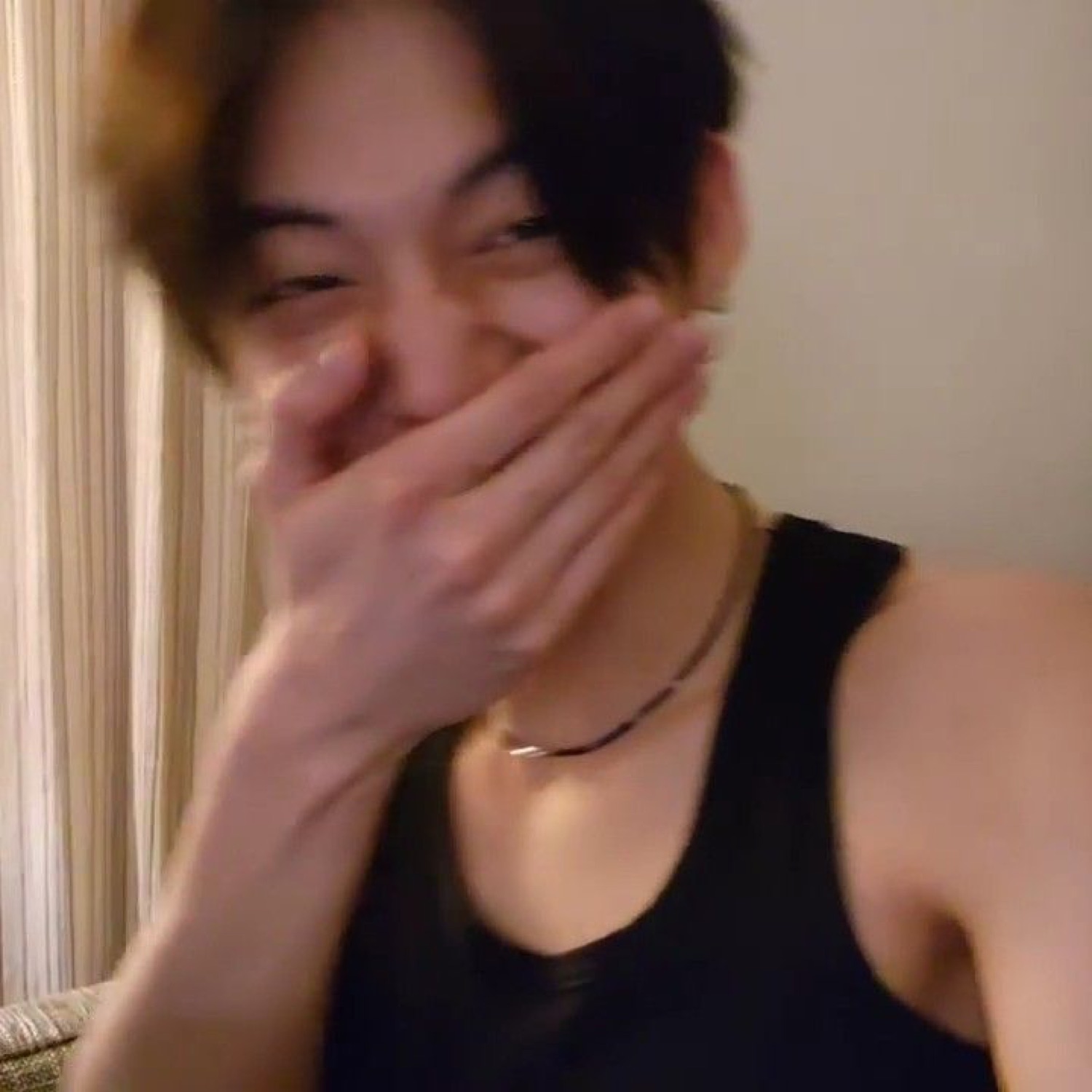 Person covering their laughing mouth with their hand, eyes scrunched shut in a giggle fit