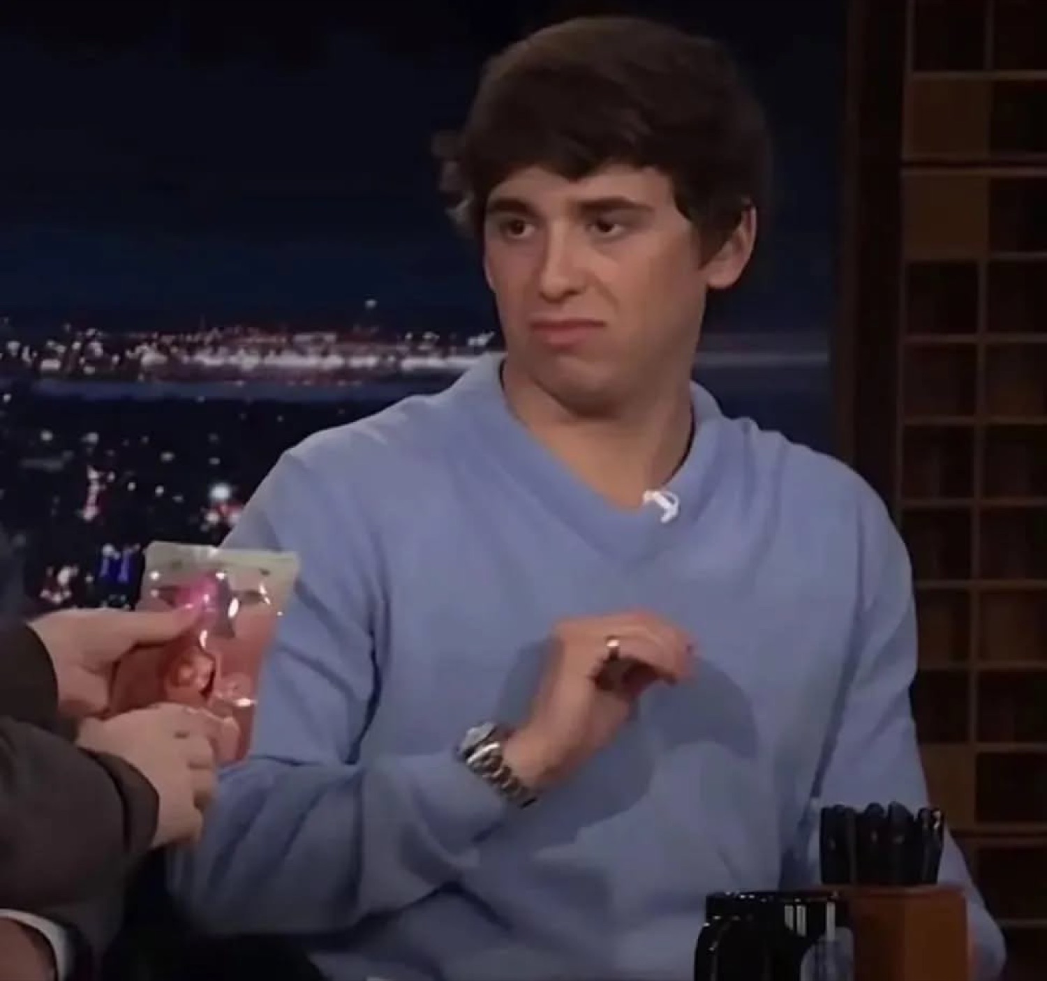 Young man in a blue sweater on a talk show giving a skeptical side glance