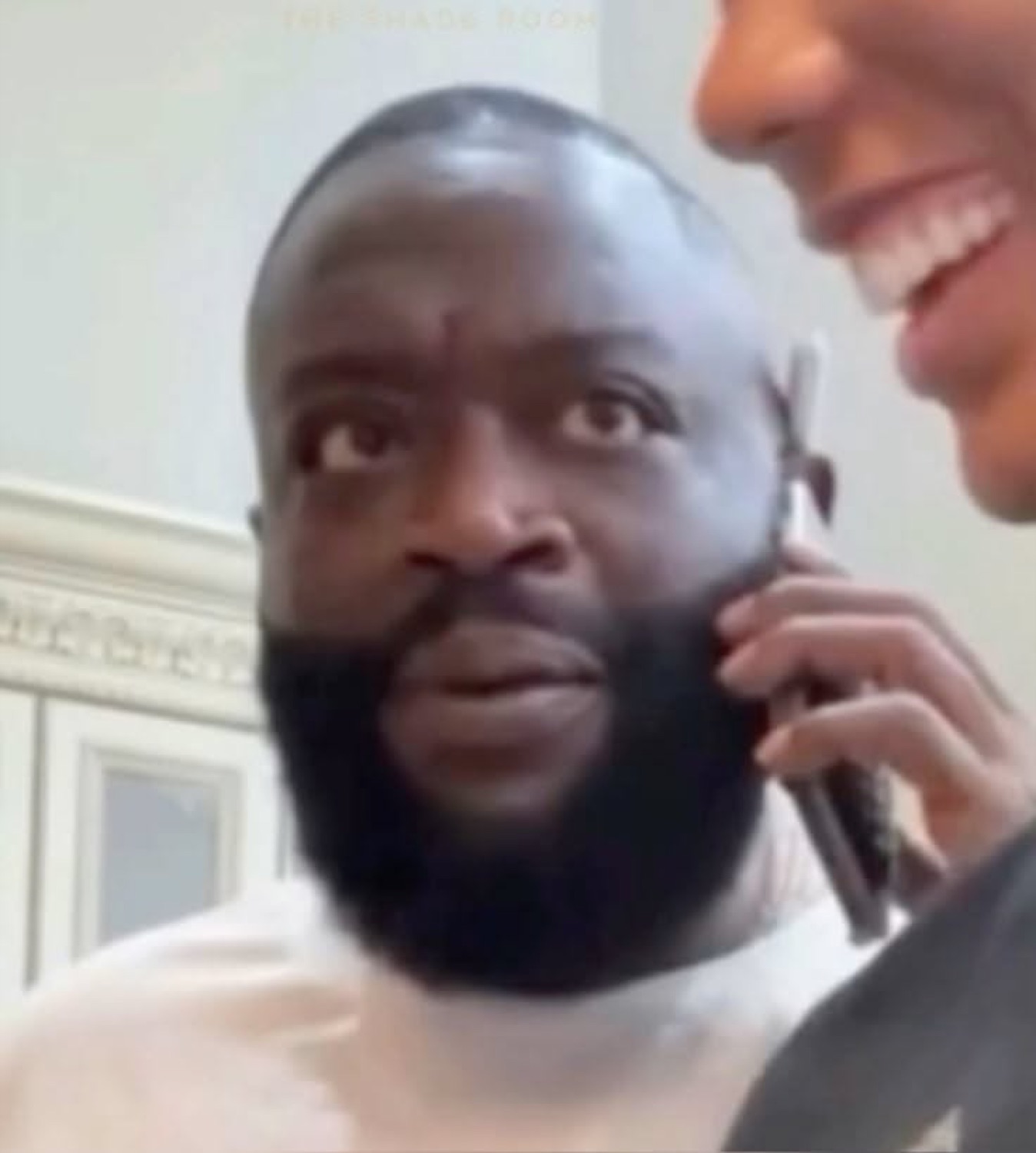Man with a large beard staring blankly ahead while someone off-frame smiles