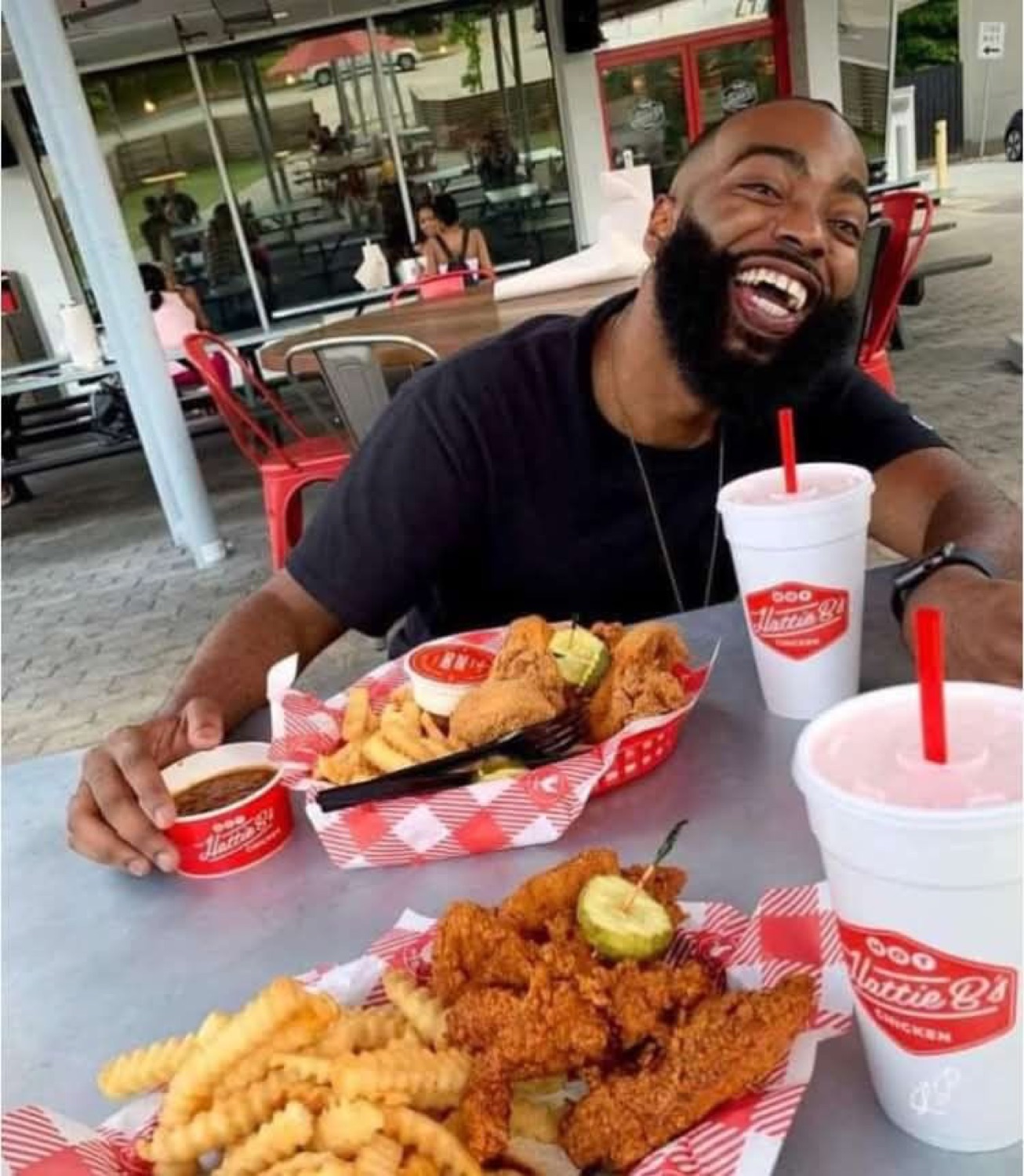 Bearded man laughing head back at a table full of fried chicken and fries at Hattie B's