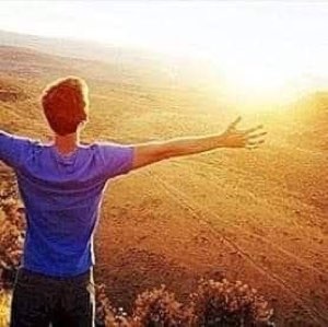 Guy from behind with arms flung wide toward a golden sunlit field, fully free