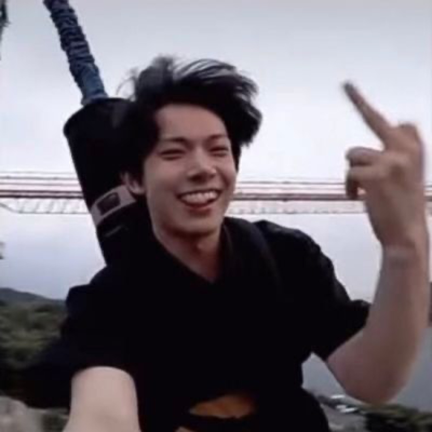 Young man grinning and flipping off the camera while strapped into a bungee jump harness