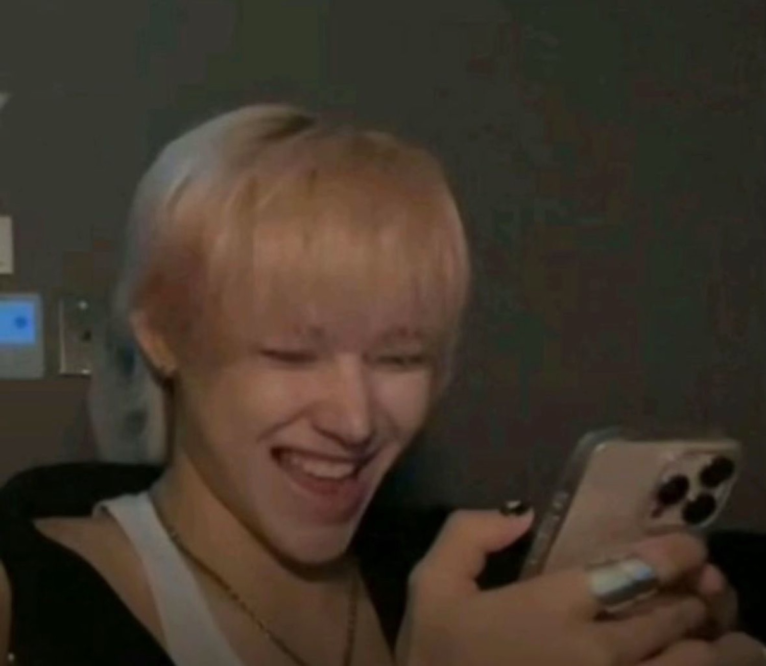 Person with platinum blonde hair laughing hard while looking at their phone