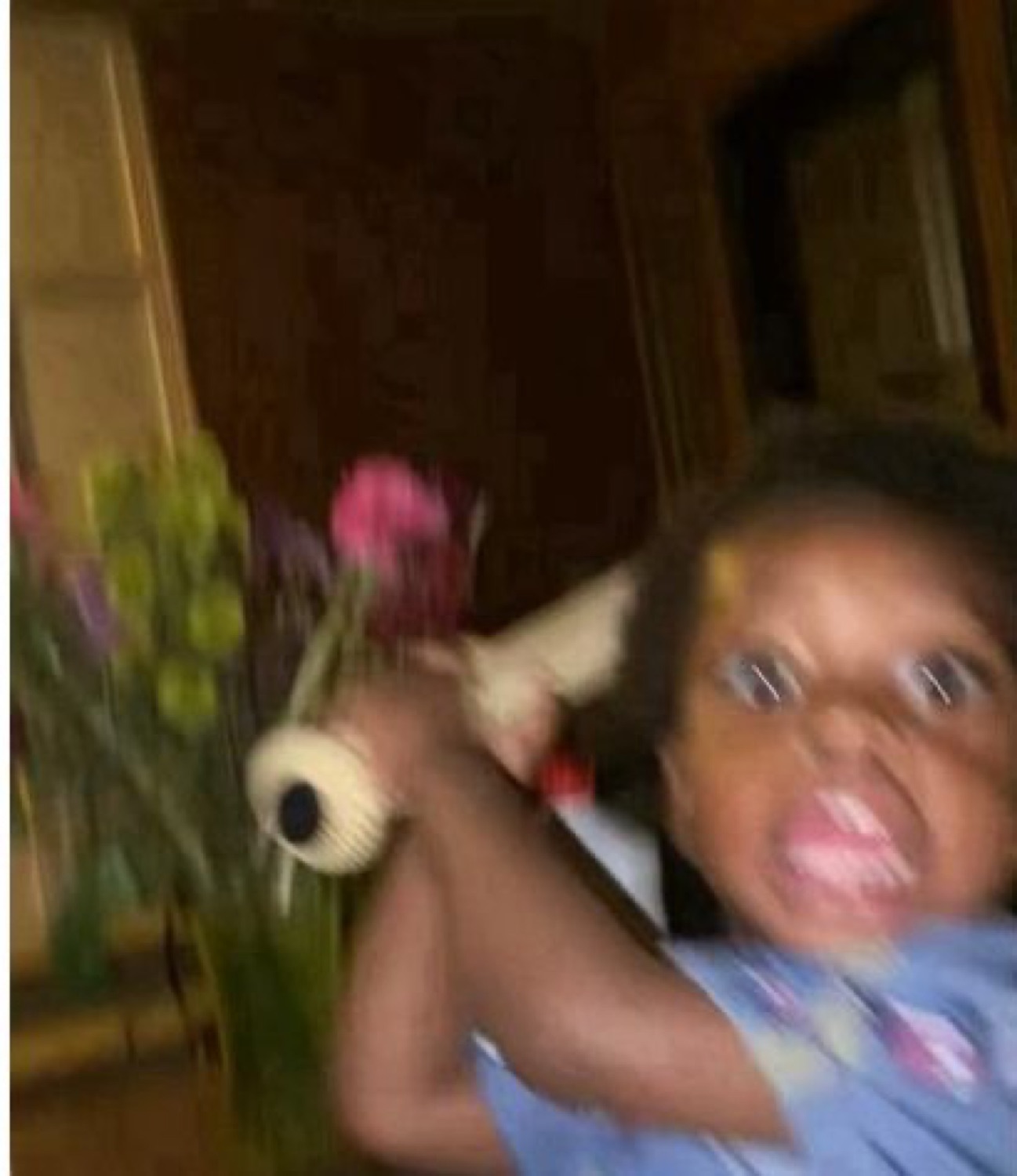 Blurry shot of a grinning toddler swinging past a vase of flowers