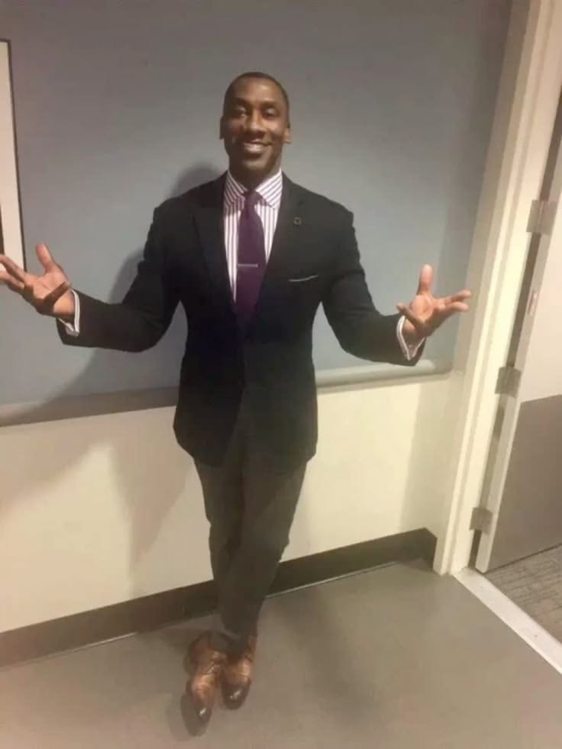 Tall man in a suit spreading his arms wide with a big grin, as if saying 'ta-da'