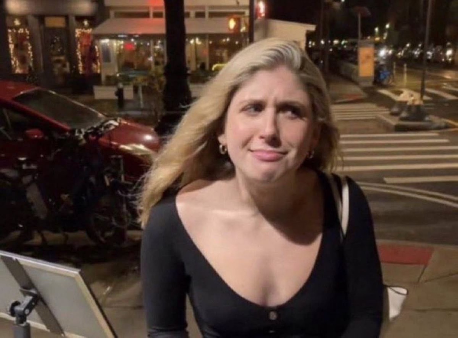 Blonde woman on a night street pulling a squinty, skeptical cringe face