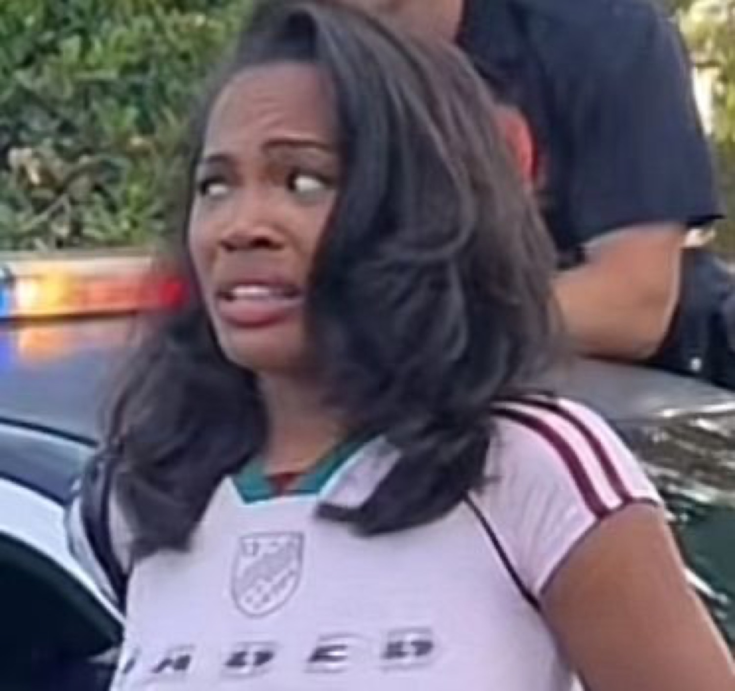 Woman by a police car pulling a full-body cringe with her eyes cut sideways