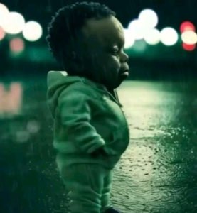 Tiny toddler in a hoodie standing alone in the rainy street lights, lip out