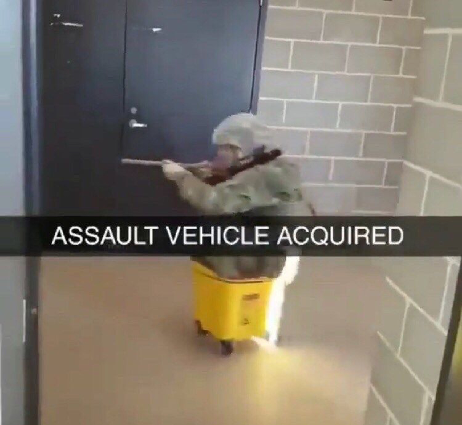 Person in camo riding a yellow mop bucket down a hall captioned 'ASSAULT VEHICLE ACQUIRED'