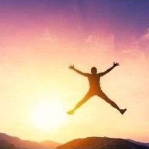 Silhouetted person leaping arms-wide against a pink and gold sunset