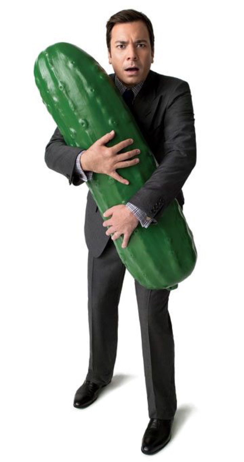 Man in a suit clutching an enormous pickle with a bewildered expression