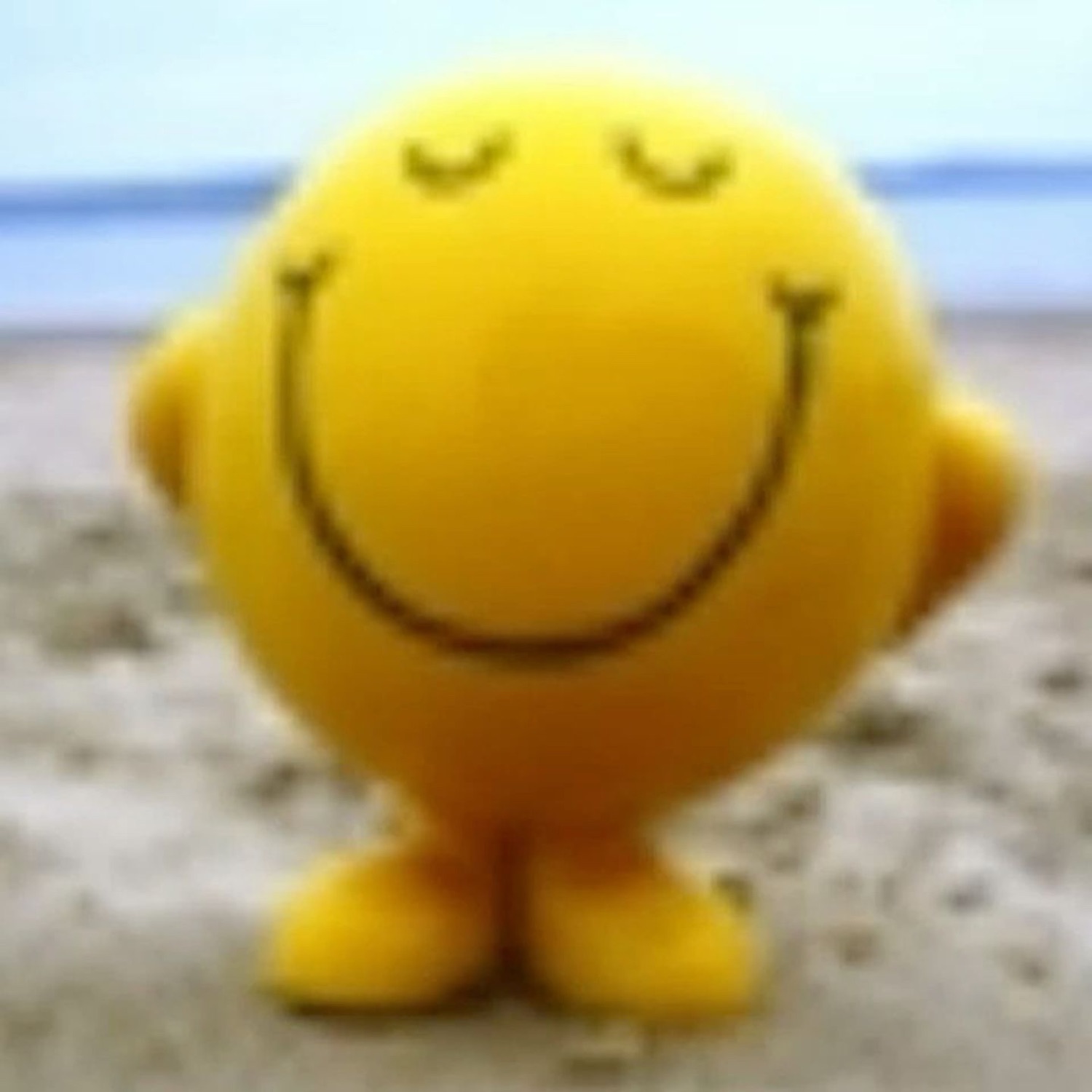 Mr. Happy smiley face toy on a beach with eyes closed and a calm contented smile